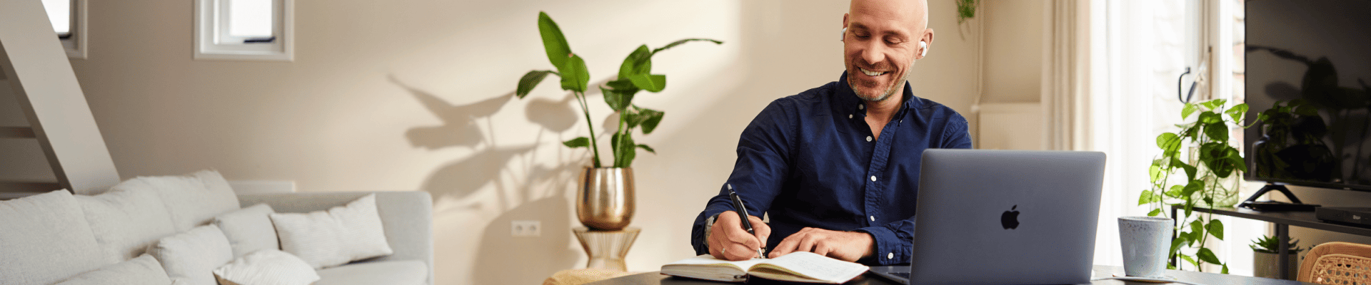 Man achter de laptop aan het schrijven in een notitieblok