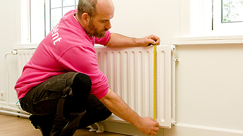 Foto: Freek meet de hoogte en breedte van de radiator met een rolmaat