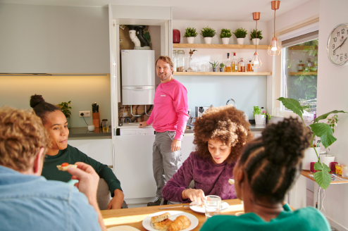 Een familie zit aan de keukentafel en de monteur van Essent staat bij de boiler in de keuken