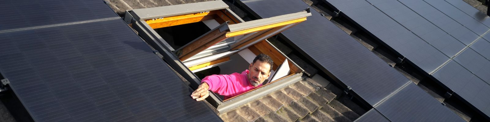 man kijkt uit zolderraam naar zonnepanelen op het dak