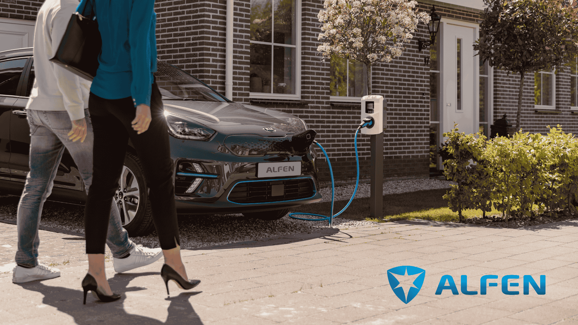 Man en vrouw lopen voor auto langs die oplaadt bij een Alfen laadpaal.