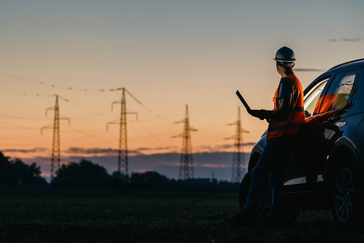 Vrouw met werkkleding aan met op de achtergrond elektrticiteitsmasten