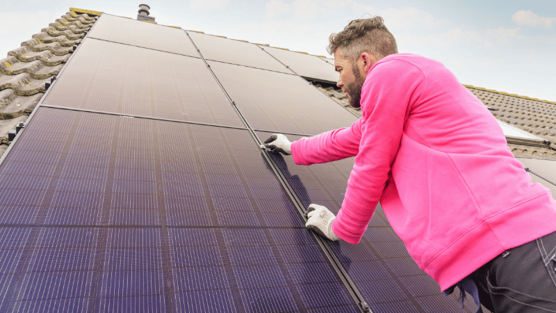 Man in essent trui installeert zonnepanelen