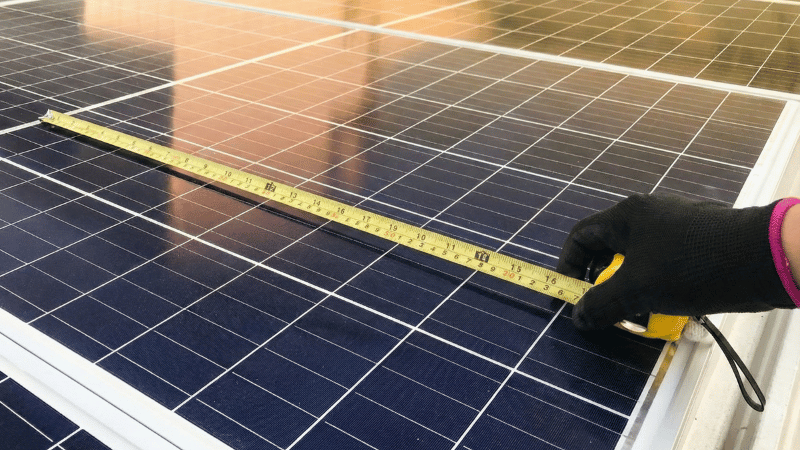 Iemand houdt een meetlat bij zonnepanelen